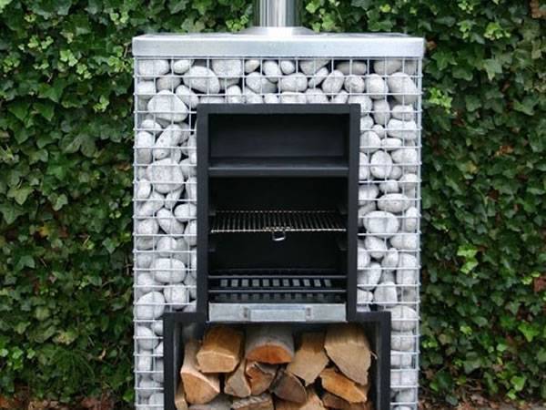 A gabion BBQ with a chimney on the top, a BBQ plate on the wood and some wood at the bottom.