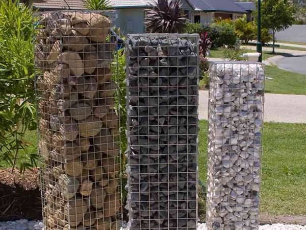 Three gabion posts is filled with different materials on pebble ground.