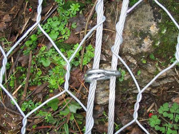 Hexagonal wire meshes are connected together by rope and clips on a mountain.